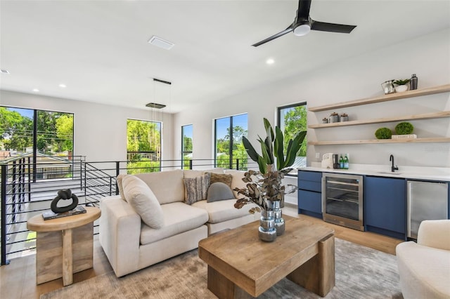 living room featuring beverage cooler, bar with sink, recessed lighting, light wood finished floors, and ceiling fan