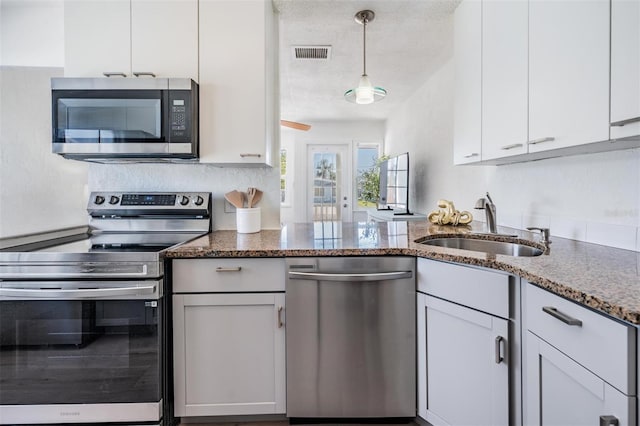 13304 2nd St E, Madeira Beach, FL 33708 - kitchen featuring stainless steel appliances, a sink, white cabinetry, dark stone countertops, and pendant lighting