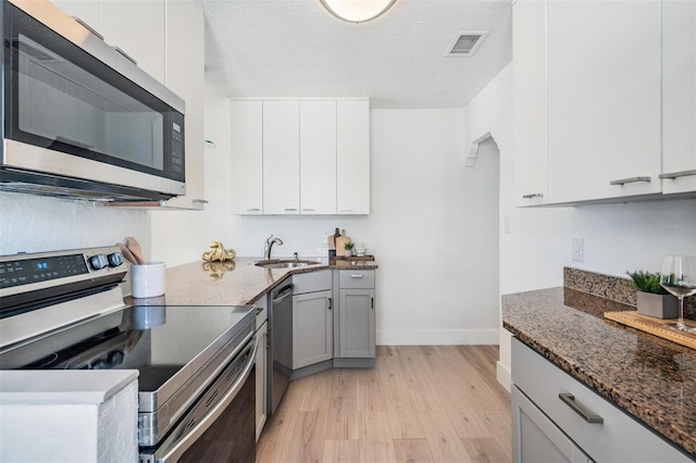 13304 2nd St E, Madeira Beach, FL 33708 - kitchen featuring appliances with stainless steel finishes, a sink, baseboards, light wood-style flooring, and dark stone counters