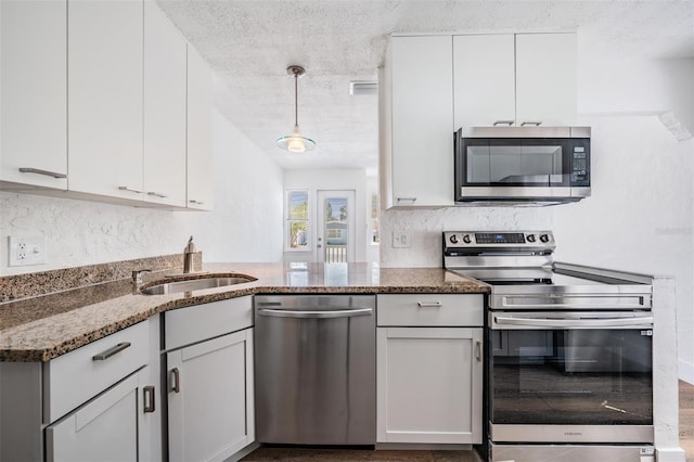 13304 2nd St E, Madeira Beach, FL 33708 - kitchen featuring appliances with stainless steel finishes, a sink, white cabinetry, a textured ceiling, and dark stone countertops
