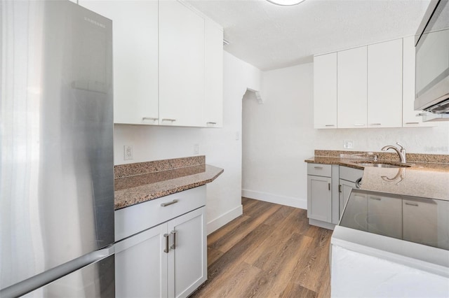 13304 2nd St E, Madeira Beach, FL 33708 - kitchen with a sink, freestanding refrigerator, light wood finished floors, light stone countertops, and white cabinets