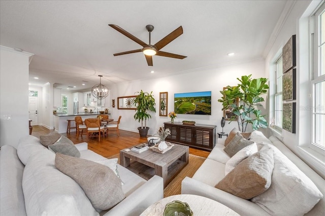 living room featuring a ceiling fan, light wood-style flooring, recessed lighting, a chandelier, and ornamental molding