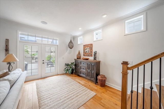 entrance foyer with ornamental molding, light wood-style floors, french doors, baseboards, and stairway