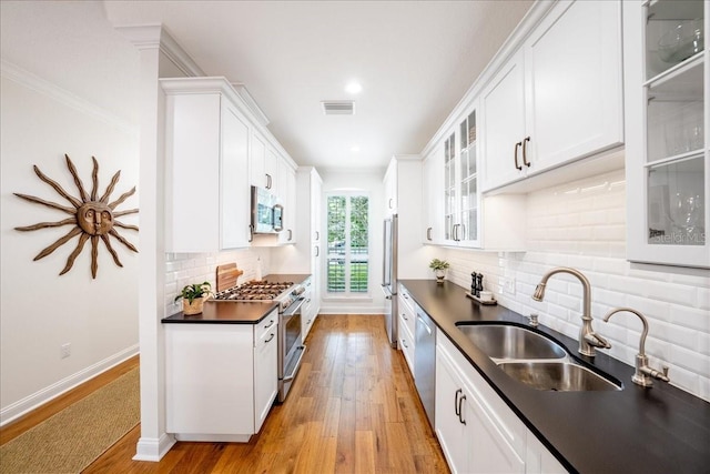 kitchen featuring high quality appliances, dark countertops, a sink, white cabinetry, and light wood-type flooring