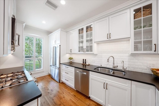 kitchen with appliances with stainless steel finishes, a sink, dark countertops, white cabinetry, and decorative backsplash
