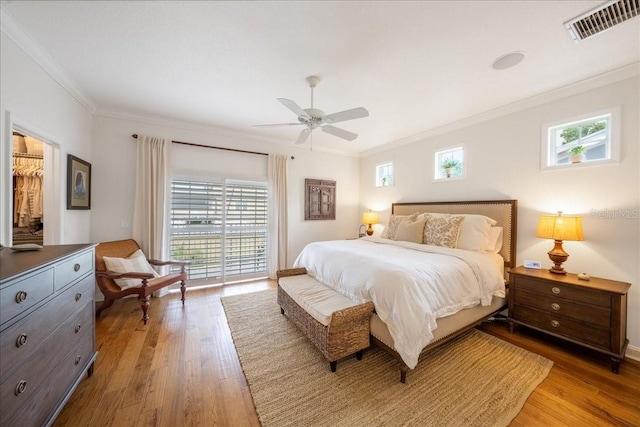 bedroom featuring light wood-type flooring, ornamental molding, multiple windows, and a ceiling fan