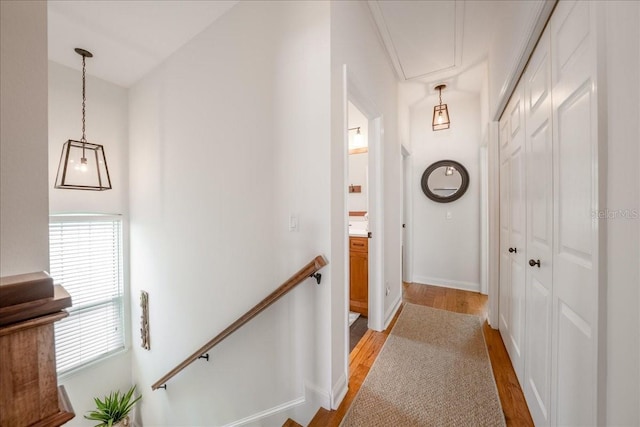 hallway with light wood finished floors, attic access, an upstairs landing, and baseboards