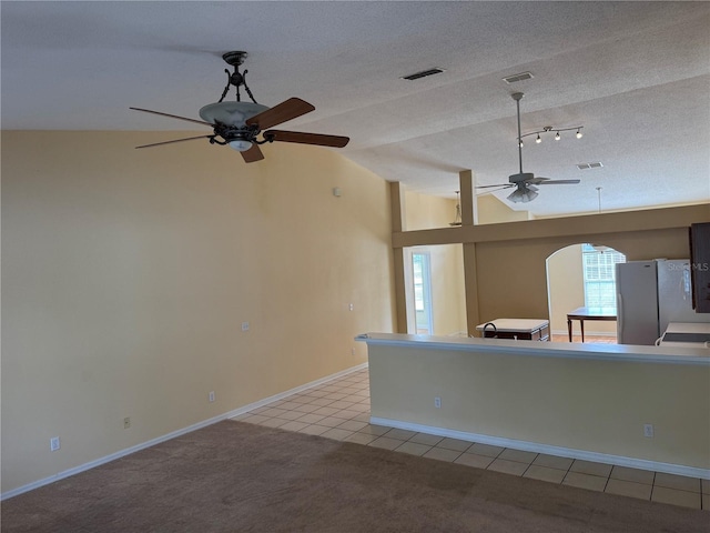 unfurnished living room featuring ceiling fan, vaulted ceiling, a textured ceiling, light tile patterned floors, and baseboards