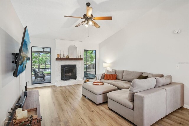 living room featuring plenty of natural light, a stone fireplace, a ceiling fan, light wood-style flooring, and vaulted ceiling