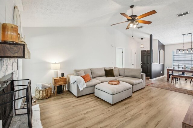 living room featuring lofted ceiling, light wood-style flooring, ceiling fan, a textured ceiling, and baseboards