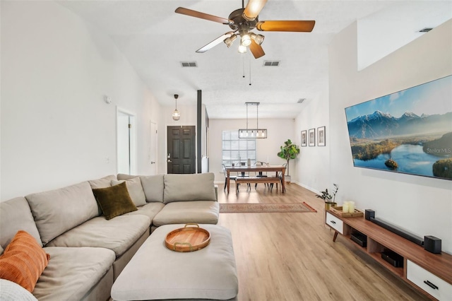 living room with light wood-style floors, a ceiling fan, a chandelier, and baseboards