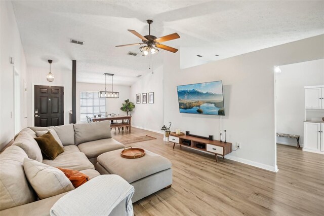 living area with light wood-type flooring, vaulted ceiling, ceiling fan, and baseboards