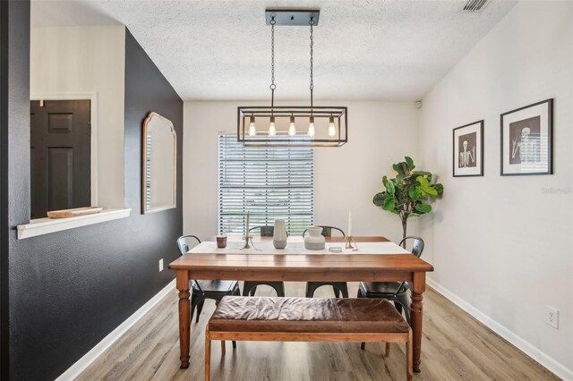 dining area with light wood-style flooring, baseboards, a textured ceiling, and a chandelier