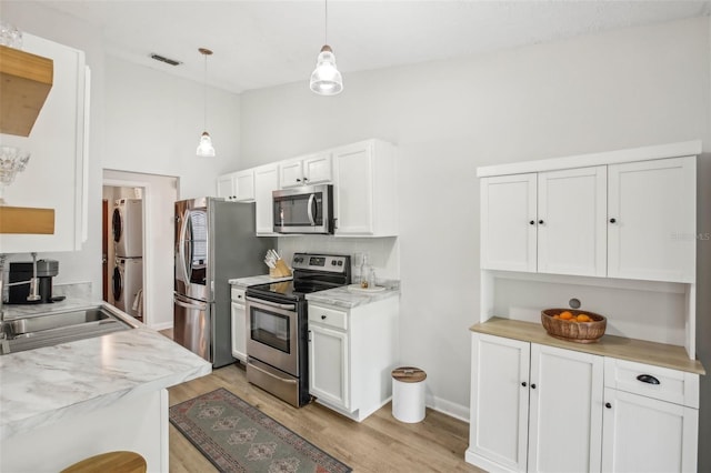 kitchen featuring appliances with stainless steel finishes, stacked washer and clothes dryer, light countertops, light wood-style floors, and lofted ceiling