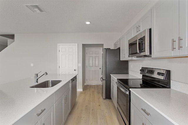 kitchen featuring stainless steel appliances, a sink, light wood-type flooring, light stone counters, and recessed lighting