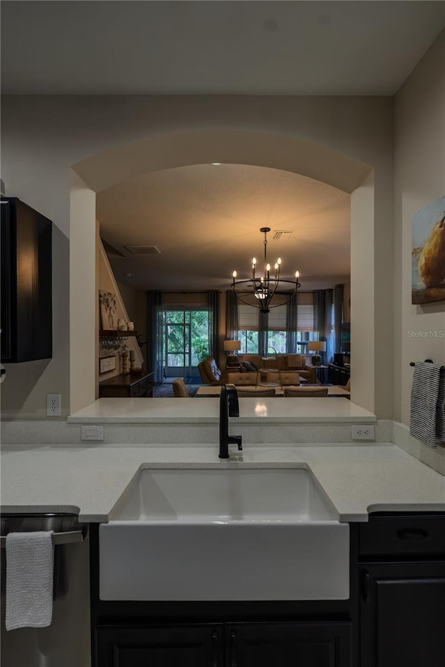 kitchen featuring a sink, dishwasher, light countertops, dark cabinets, and a chandelier