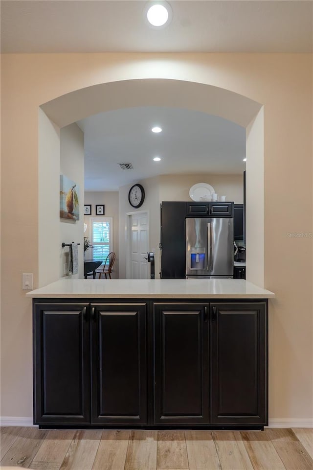 kitchen with stainless steel refrigerator with ice dispenser, dark cabinets, arched walkways, light countertops, and recessed lighting