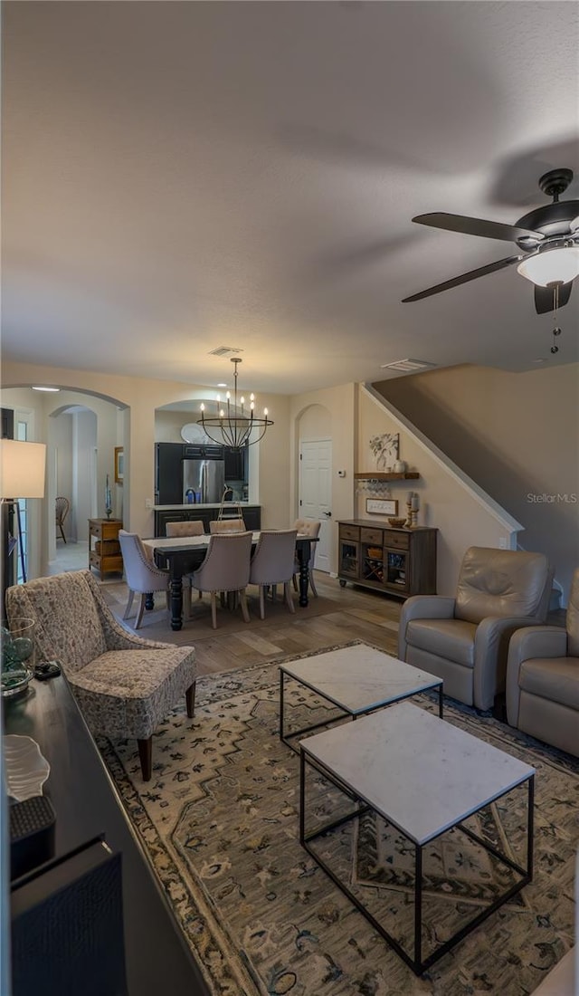 living room featuring arched walkways, ceiling fan, wood finished floors, and a chandelier