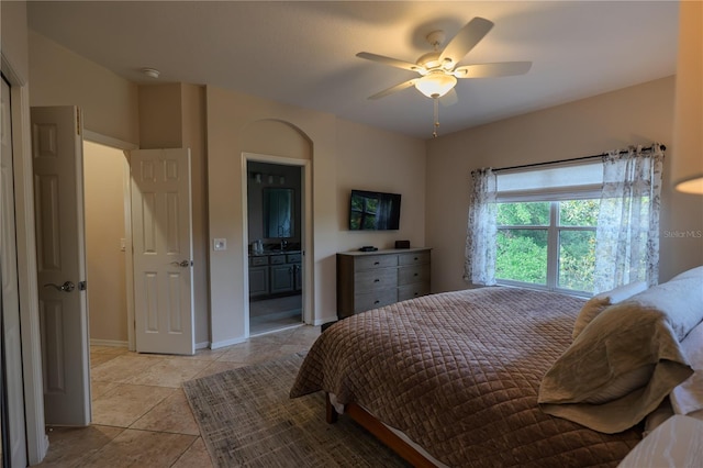 bedroom featuring light tile patterned flooring, a ceiling fan, ensuite bath, and baseboards