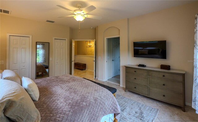 bedroom featuring two closets, light tile patterned floors, a ceiling fan, and baseboards