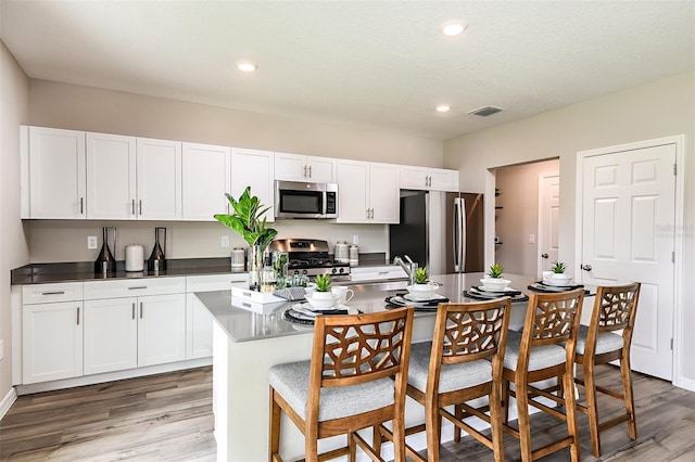 kitchen with appliances with stainless steel finishes, light wood-style flooring, white cabinetry, a breakfast bar, and a center island with sink
