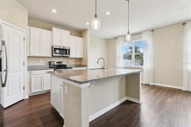 392 Summer Squall Rd, Davenport, FL 33837 - kitchen with appliances with stainless steel finishes, a sink, dark wood-style flooring, light stone counters, and an island with sink