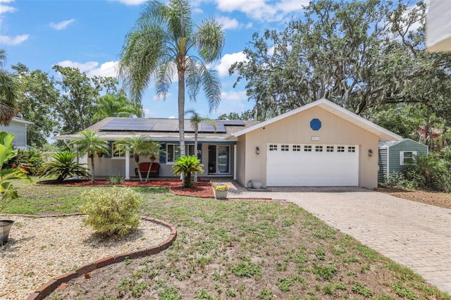 ranch-style house with an attached garage, decorative driveway, solar panels, and a front lawn