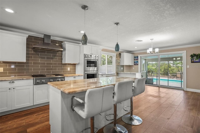 kitchen featuring appliances with stainless steel finishes, wall chimney exhaust hood, ornamental molding, dark wood-type flooring, and white cabinets