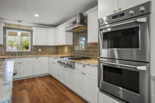kitchen featuring stainless steel appliances, wall chimney range hood, a sink, white cabinets, and light stone counters