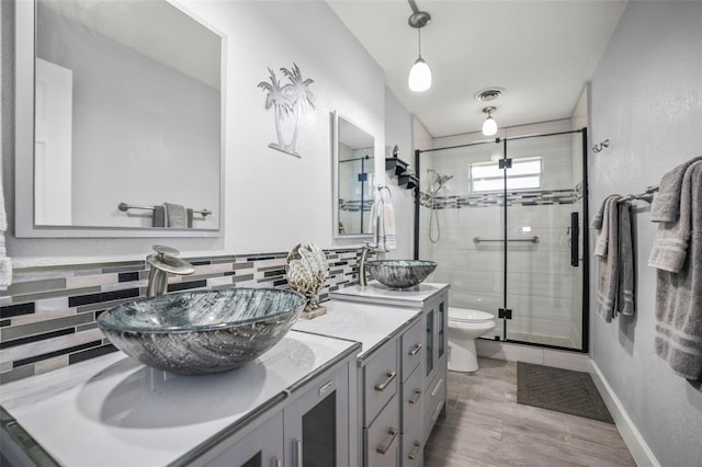 bathroom with a stall shower, backsplash, toilet, double vanity, and wood finished floors