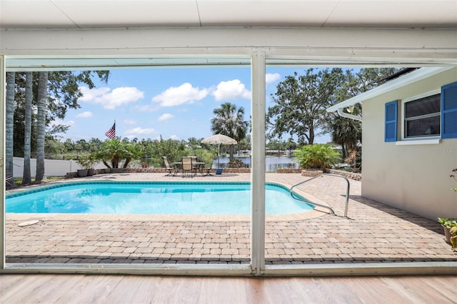 outdoor pool featuring a patio, a water view, and fence
