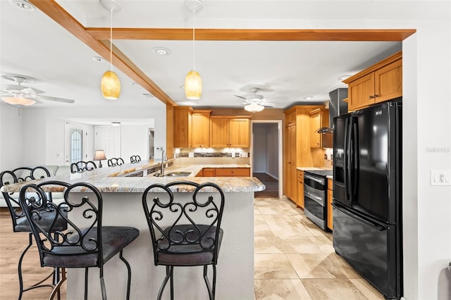 kitchen featuring black refrigerator with ice dispenser, a ceiling fan, stainless steel range with electric stovetop, a kitchen bar, and a sink