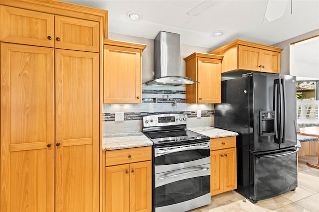 kitchen featuring wall chimney range hood, black refrigerator with ice dispenser, range with two ovens, decorative backsplash, and light stone counters