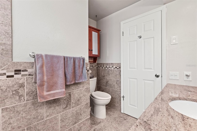 bathroom featuring tile walls, tile patterned flooring, toilet, wainscoting, and vanity