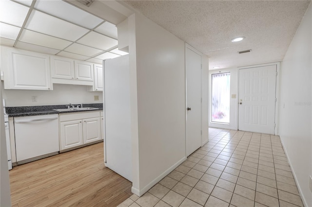 kitchen featuring white dishwasher, a sink, dark countertops, white cabinets, and a textured ceiling