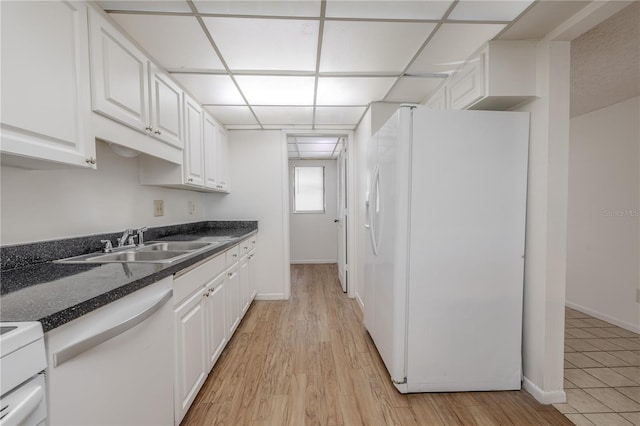 kitchen featuring white appliances, a sink, white cabinets, dark countertops, and light wood-style flooring
