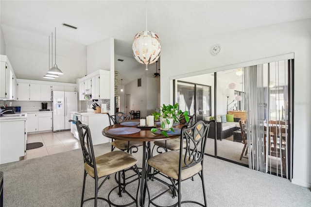 dining space featuring vaulted ceiling, light carpet, and light tile patterned flooring