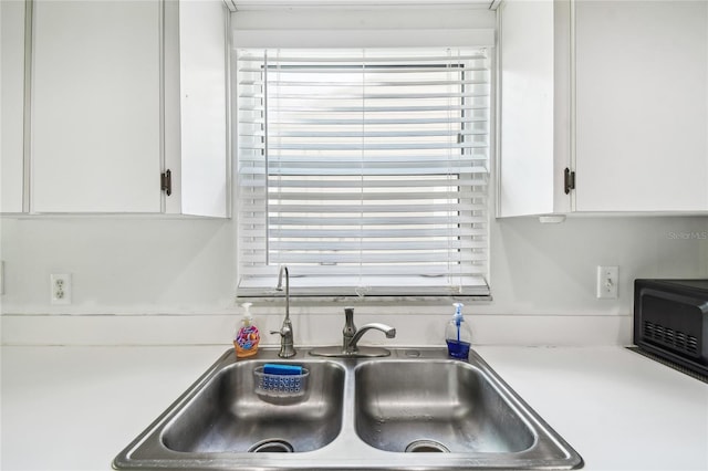 kitchen view of a sink, white cabinetry, and light countertops