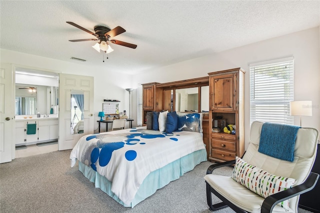 bedroom featuring light colored carpet, a textured ceiling, ensuite bath, and a ceiling fan