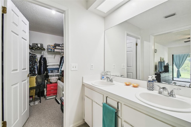 bathroom with a textured ceiling, double vanity, and a walk in closet