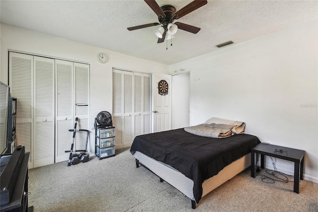 bedroom featuring carpet flooring, two closets, a textured ceiling, and a ceiling fan