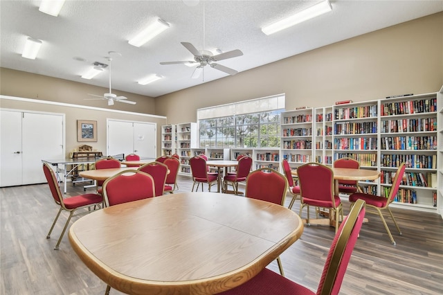dining space featuring wood finished floors, a ceiling fan, a textured ceiling, and a high ceiling