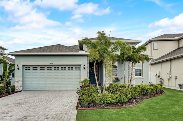 view of front of property with decorative driveway, stucco siding, an attached garage, a front lawn, and stone siding