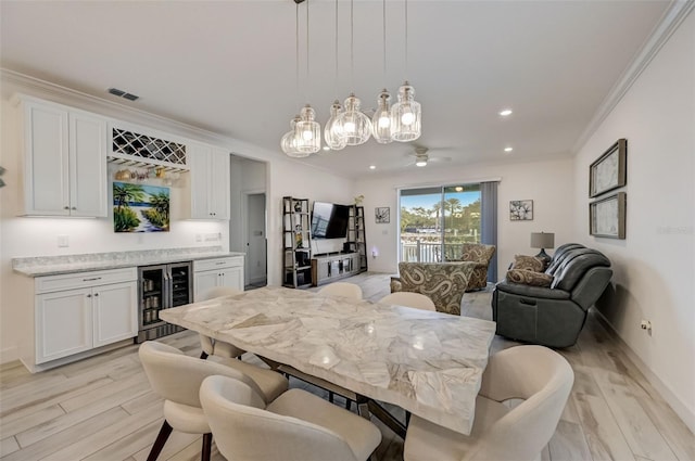dining area featuring wine cooler, a bar, crown molding, light wood-style flooring, and ceiling fan