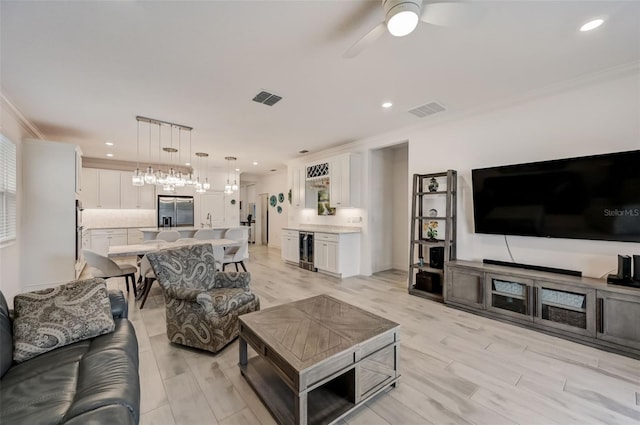 living room featuring wine cooler, crown molding, a ceiling fan, light wood finished floors, and recessed lighting