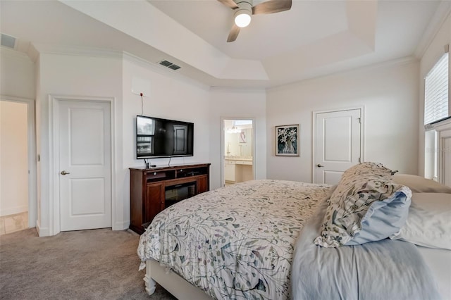 carpeted bedroom with a tray ceiling, crown molding, ceiling fan, ensuite bath, and baseboards