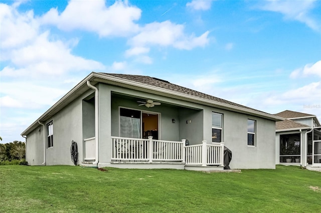 rear view of property featuring stucco siding, a yard, and a ceiling fan