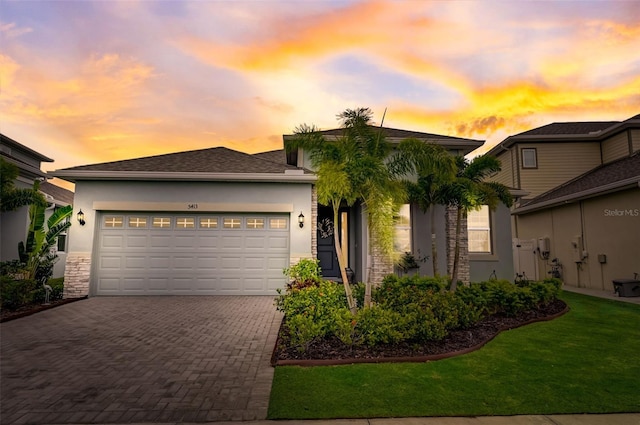 view of front of house with decorative driveway, stucco siding, an attached garage, stone siding, and a lawn