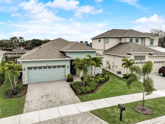 view of front of property featuring an attached garage, decorative driveway, a shingled roof, a front lawn, and stucco siding