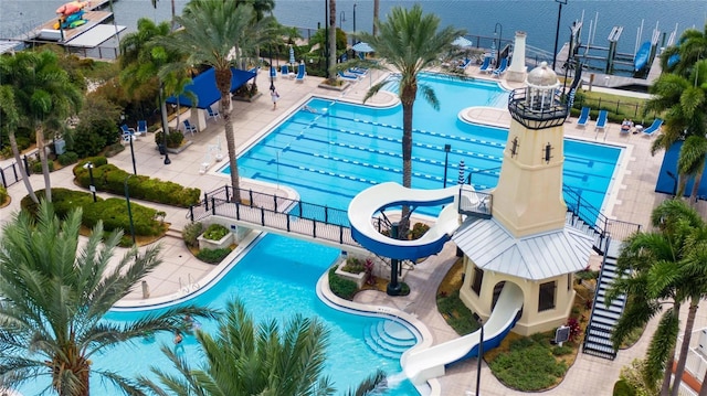 community pool with a water slide, fence, and a patio area